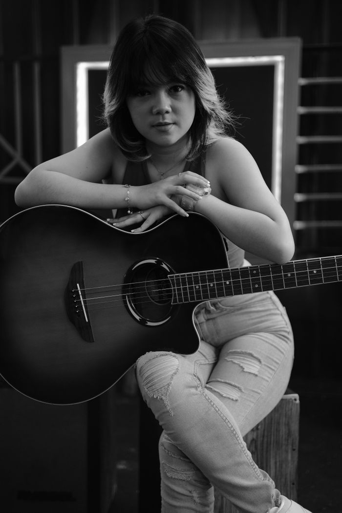 our-experience Black and white portrait of a woman with an acoustic guitar, creating a moody musical ambiance.