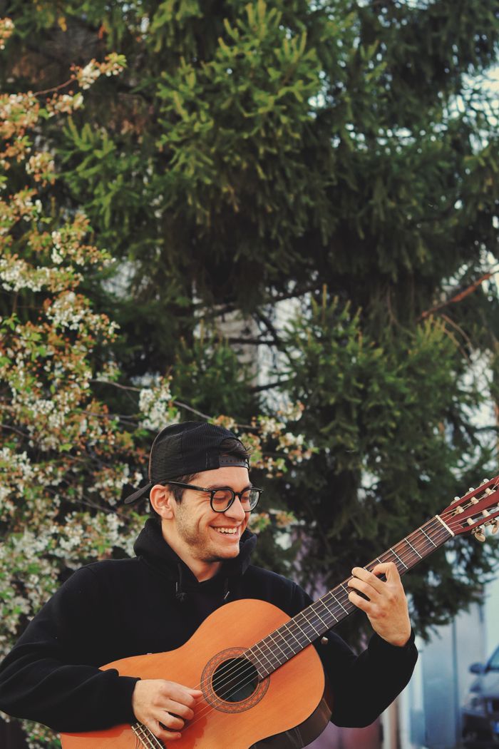 why-choose-us Smiling young man in eyeglasses and cap playing acoustic guitar under branches of blooming tree