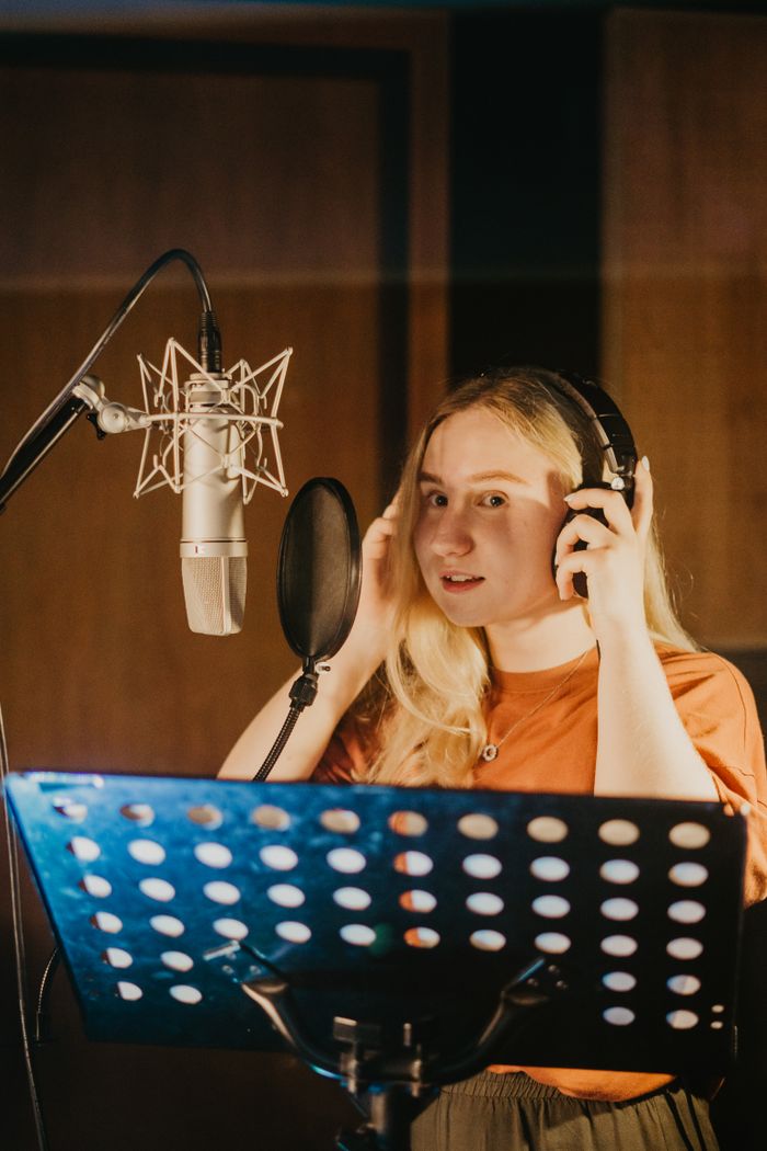 services-01 A female singer in a recording studio adjusting her headphones during a music session.