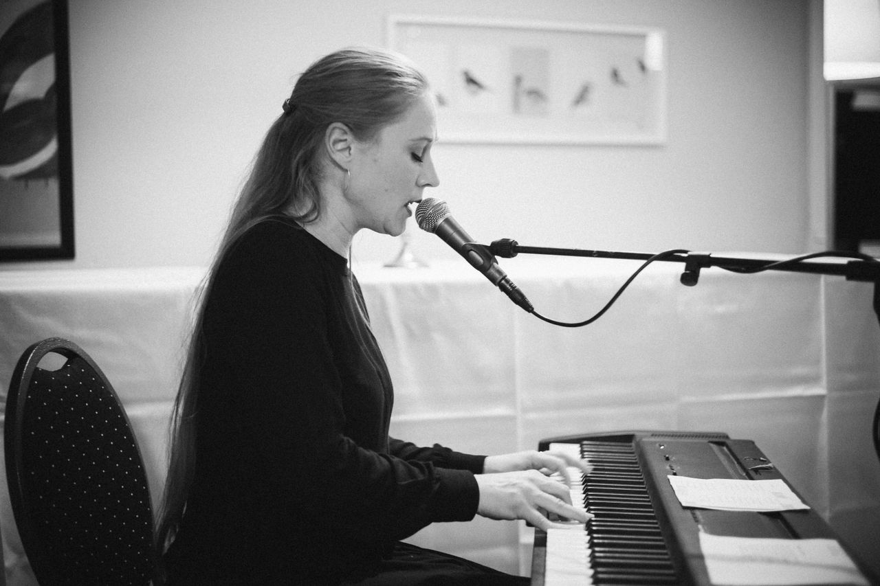 services-02 Black and white photo of a woman singing and playing the piano indoors.