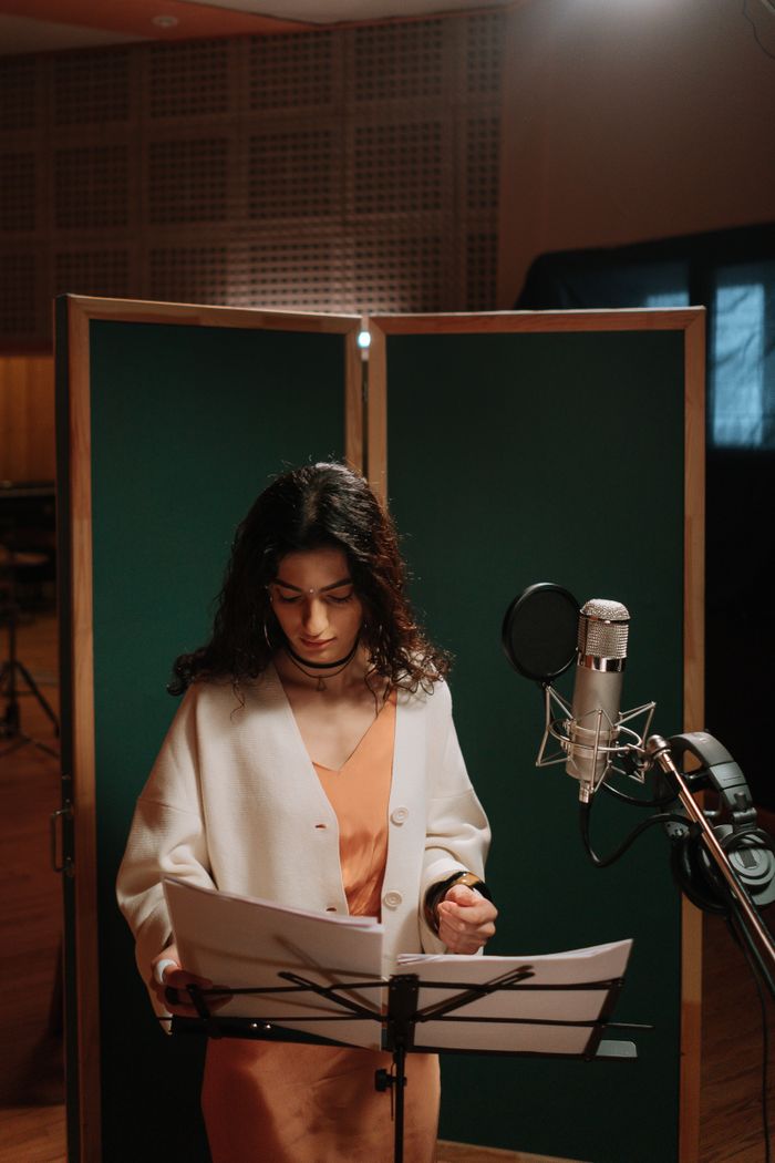 gallery-1 A female singer in a recording studio with microphone and music stand.