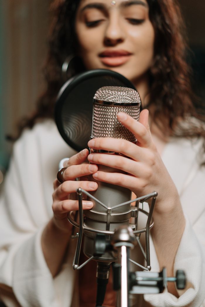 gallery-5 Close-up of a woman singing into a condenser microphone in a recording studio.