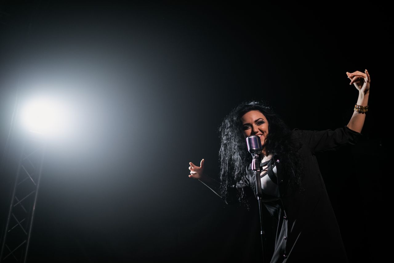 gallery-6 A vibrant female singer passionately performing under a spotlight on stage.