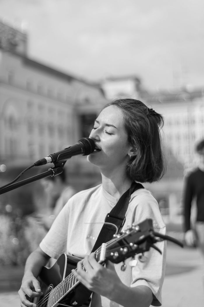 services-03 Woman sings passionately while playing guitar outdoors.